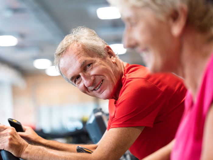 older man on exercise machine smiling at person next to him