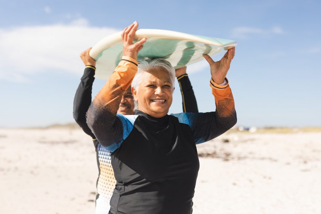 Happy mature woman carrying a surfboard for a story on good things about getting older