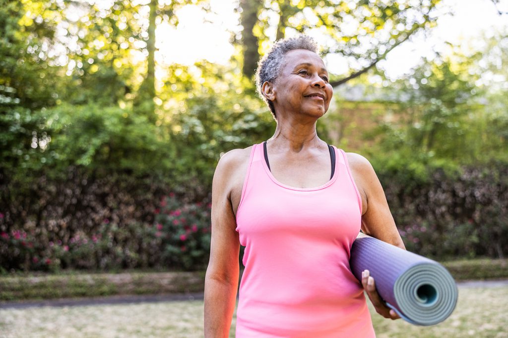 happy senior woman holding a yoga mat for a story on yoga therapy